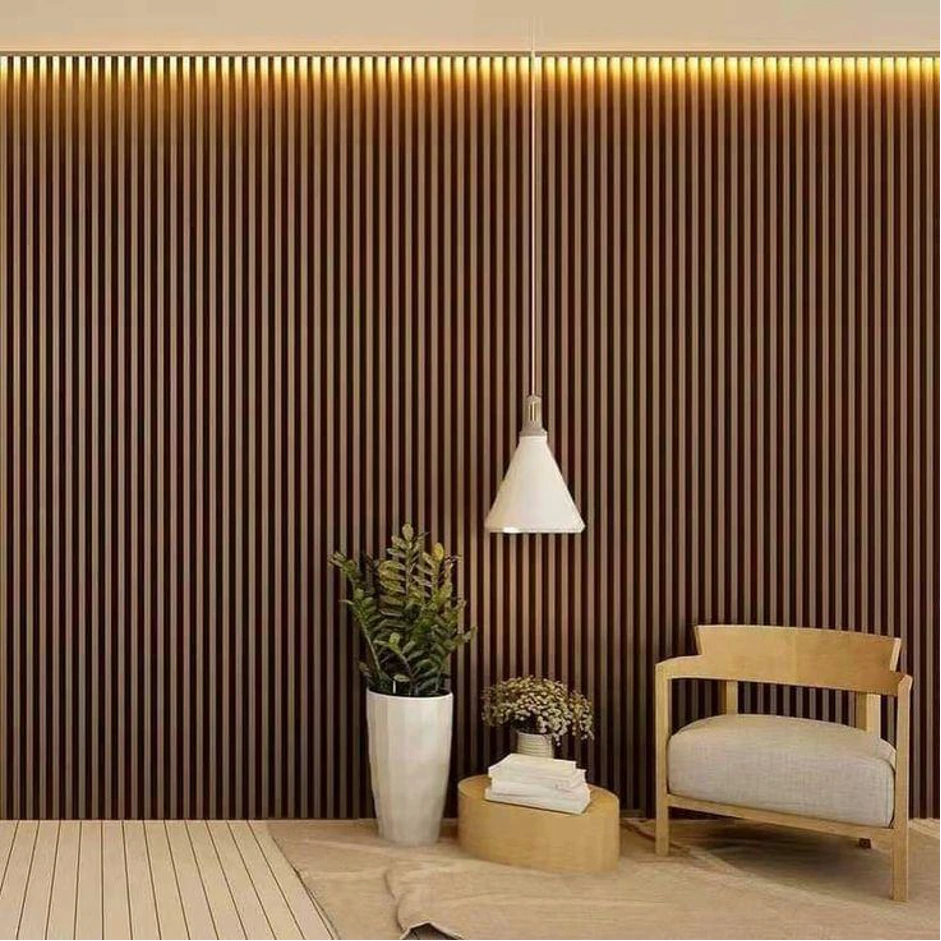 Wall panel dinding WPC vertical berwarna cokelat dengan lampu LED warm di bagian atas, dilengkapi kursi kayu, lampu gantung putih, karpet beige, dan dekorasi tanaman indoor.
